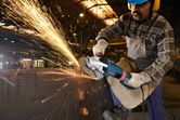 A person wearing safety equipment grinds metal, creating a shower of bright sparks.