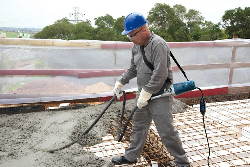 A person wearing safety equipment operates a concrete vibrator on a construction site.