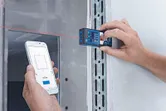 A person uses a laser measure to record distance data on a smartphone.