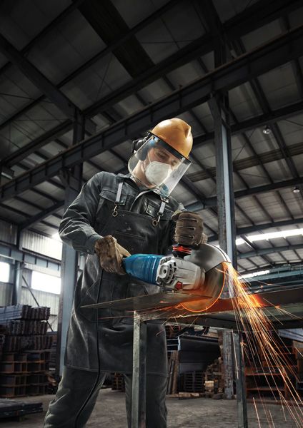 A person wearing safety equipment cuts metal with an angle grinder, creating sparks.