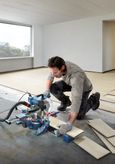 A person wearing safety equipment uses a miter saw to cut laminate flooring.