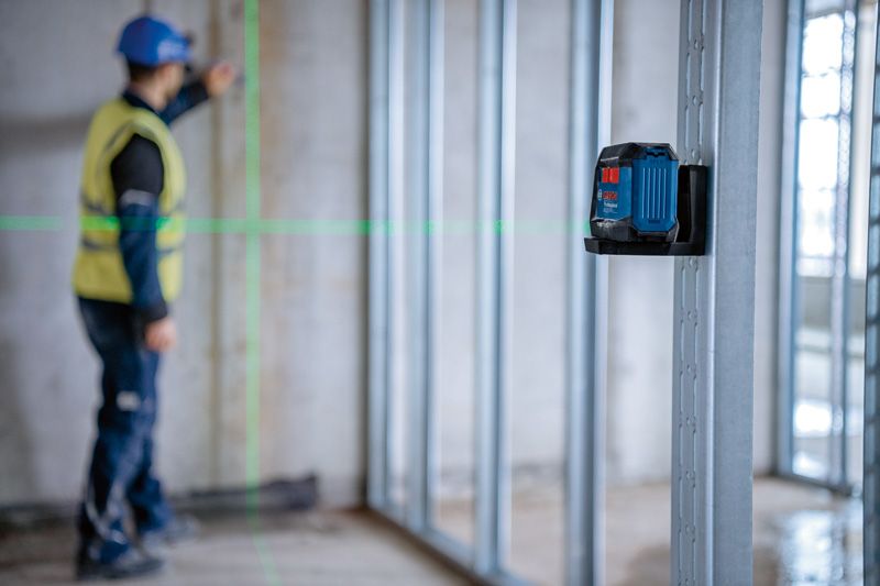 A person wearing safety equipment aligns a wall frame using a laser leveling tool.