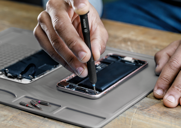 Person repairing a smartphone on a work mat using a precision screwdriver.