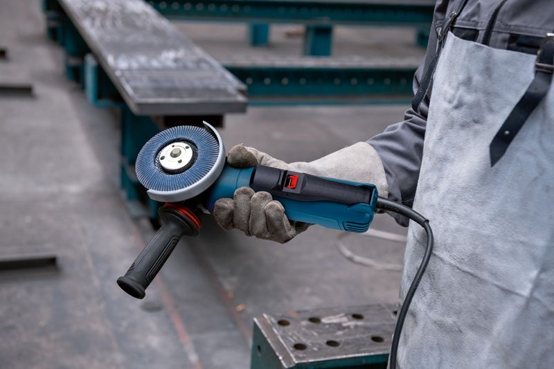 A person wearing safety equipment holds an angle grinder in an industrial setting.