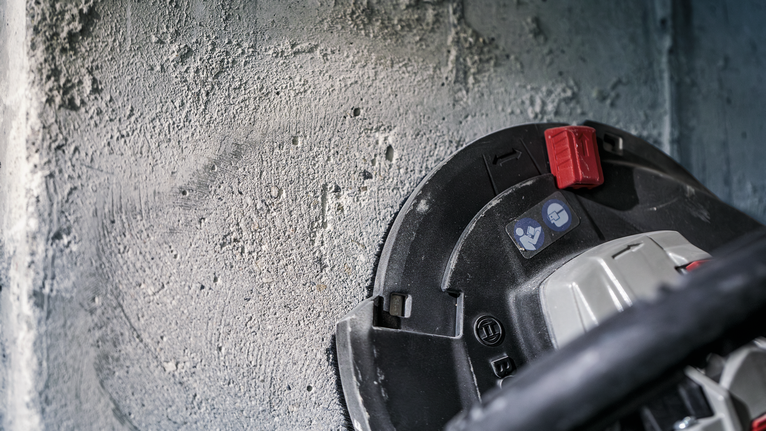 Power tool with dust extraction system working on a rough concrete wall.