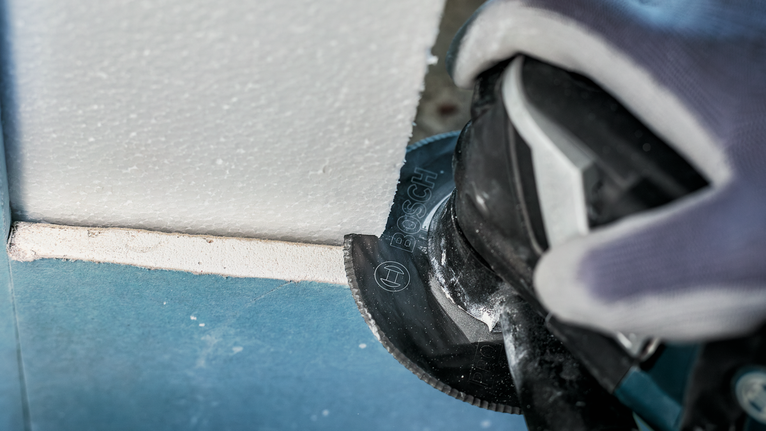 Person wearing safety equipment cuts plasterboard with a power tool.