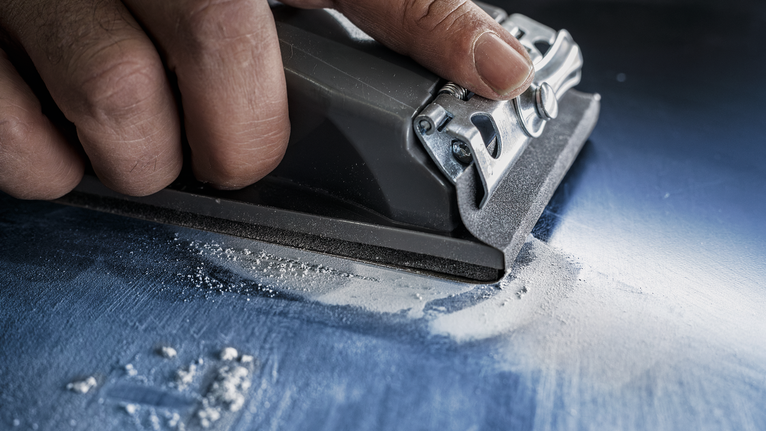 Person using a power sander to smooth a flat blue surface.
