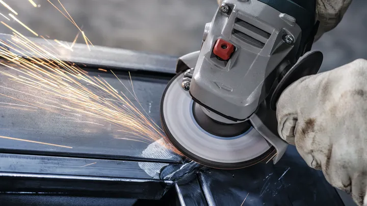 Person wearing safety equipment grinds metal, creating bright sparks.