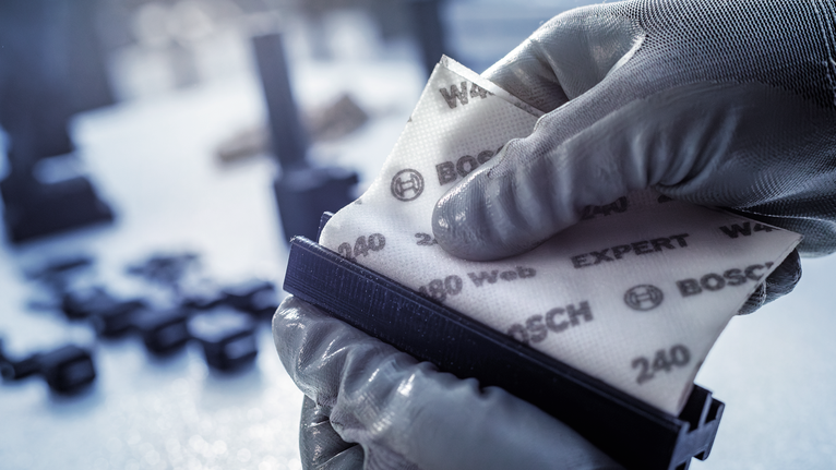 Person wearing safety equipment attaches abrasive sandpaper to a sanding block.