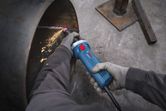 A person wearing safety equipment uses a straight grinder to grind the edge of a metal pipe.