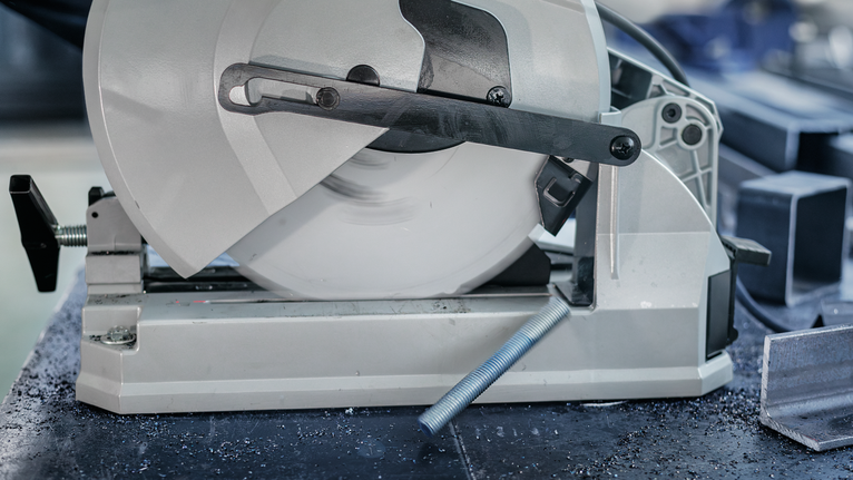 Metal cutting saw slicing through a steel rod in a workshop.