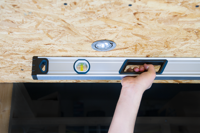 Person using a spirit level to check alignment of a wooden ceiling panel.