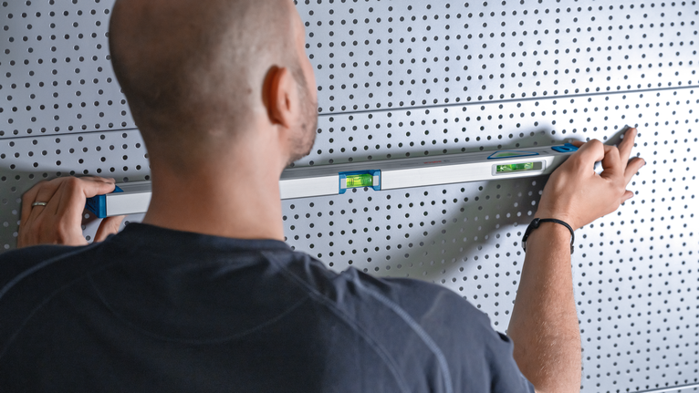 Person adjusts a spirit level on a perforated metal wall.