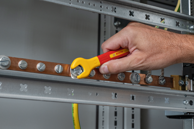 Person tightens a metal bolt on an electrical rail using an insulated wrench.