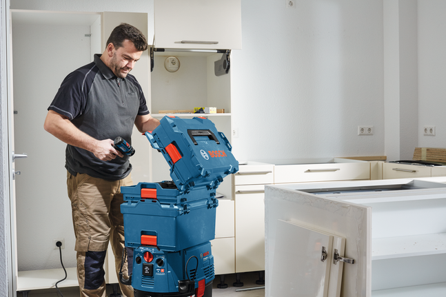 Person using a cordless tool and opening a blue tool storage box in a kitchen under renovation.