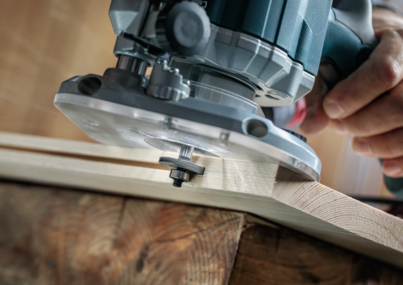 Person guides a power router along the edge of a wooden board.