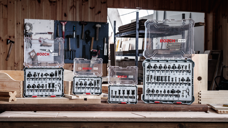 Four organized drill bit sets displayed on a wooden workbench in a workshop.
