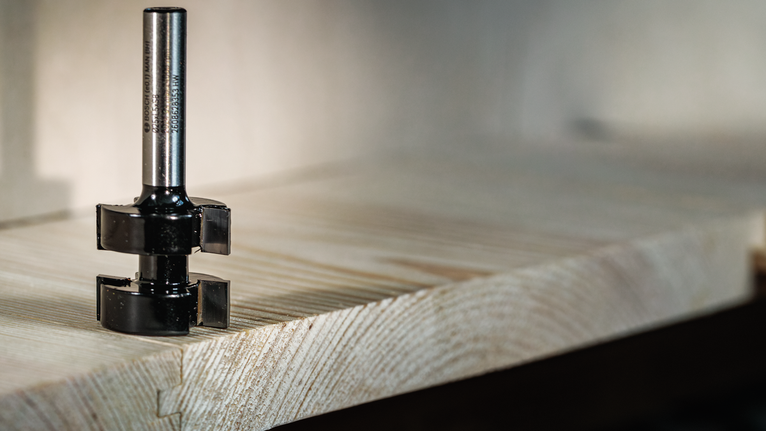 Forstner bit resting on the edge of a wooden plank in a workshop setting.