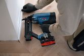 A person wearing safety equipment uses a cordless nailer to fasten floor trim.