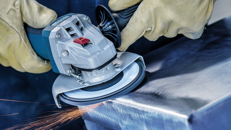Person wearing safety equipment grinds a metal surface with an angle grinder.