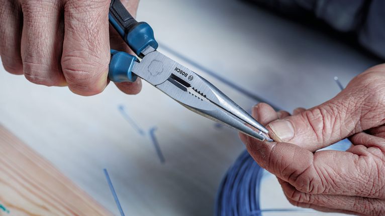 Person uses long-nose pliers to twist a small wire.