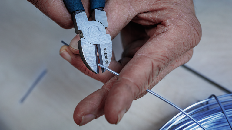 Person cutting a metal wire with pliers.