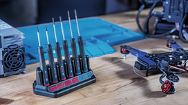Precision screwdrivers in a charging dock on a workbench beside an electronics project.