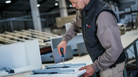 Person assembles furniture with a screwdriver at a workbench in a warehouse.