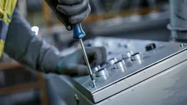 Person wearing safety equipment fastens a screw on a control panel with a screwdriver.