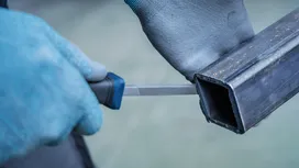 Person wearing safety equipment files the edge of a metal pipe.