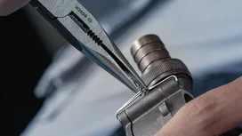 Person uses pliers to bend a metal wire on a mechanical part.
