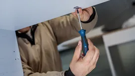 Person fastening a screw under a cabinet with a screwdriver.