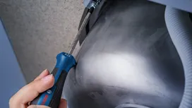 Person using a screwdriver to tighten a screw under a metal sink.