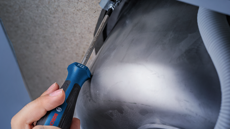 Person using a screwdriver to tighten a screw under a metal sink.