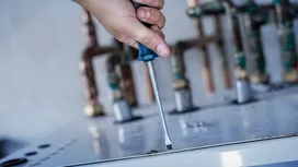 Person using a screwdriver to fasten a screw on a metal surface.