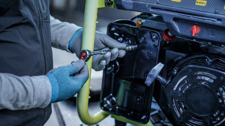 Person wearing safety equipment uses a ratchet wrench to tighten a bolt on machinery.