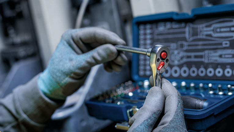 Person wearing safety equipment uses a ratchet wrench near a tool kit.