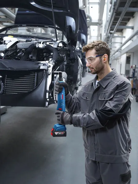 Una persona que usa equipo de seguridad aprieta los tornillos del chasis de un automóvil utilizando una herramienta eléctrica inalámbrica.