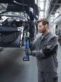 Una persona que usa equipo de seguridad aprieta los tornillos del chasis de un automóvil utilizando una herramienta eléctrica inalámbrica.