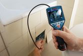 Una persona utiliza una cámara de inspección para revisar las tuberías que se encuentran detrás de los azulejos del baño.