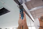 Una persona que usa equipo de seguridad corta un panel de techo con un cortador múltiple cerca de una estructura de metal.
