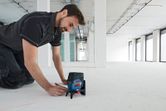 Una persona utiliza una herramienta niveladora láser con un accesorio para marcar líneas en un piso de construcción.