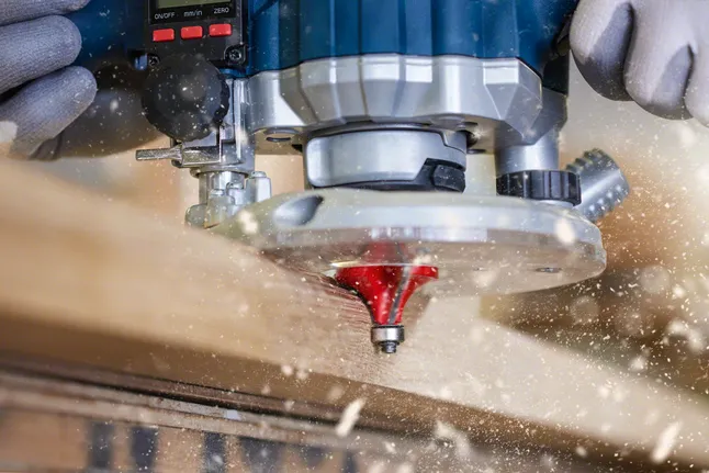 Una persona que lleva equipo de seguridad utiliza una fresadora para dar forma al borde de una tabla de madera.