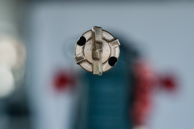 Primer plano de una broca para taladro percutor con una herramienta borrosa al fondo.