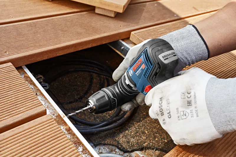 Una persona que usa equipo de seguridad utiliza un taladro atornillador inalámbrico sobre una plataforma de madera.