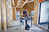 Una persona que usa equipo de seguridad corta madera con una sierra ingletadora inalámbrica en una casa en construcción.
