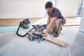 Una persona que usa equipo de seguridad corta una tabla de madera con una sierra ingletadora inalámbrica.