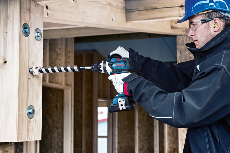 Una persona que usa equipo de seguridad perfora una viga de madera en un sitio de construcción.