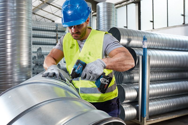 Una persona que usa equipo de seguridad fija conductos de metal utilizando una herramienta eléctrica inalámbrica.