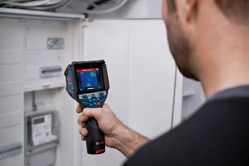 Una persona utiliza una cámara térmica para inspeccionar un panel eléctrico.